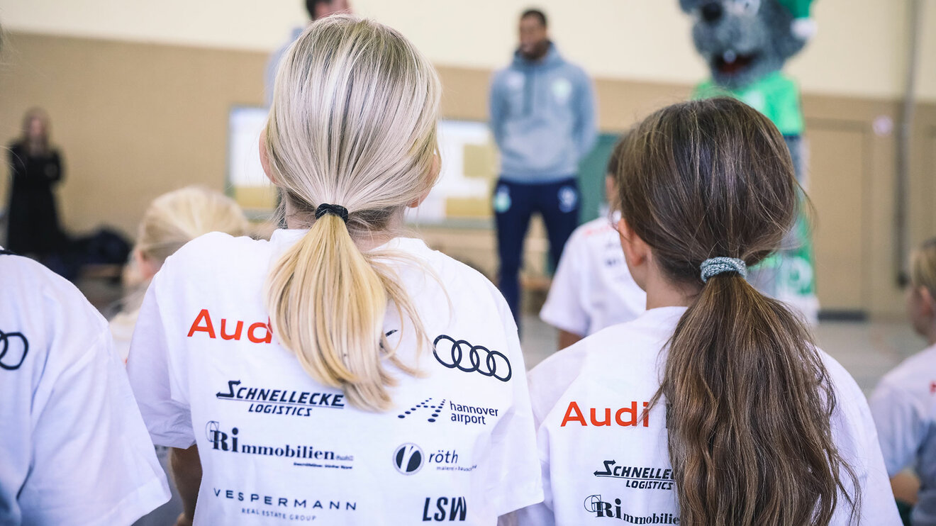 Zwei Mädchen bei der Schul-AG des VfL Wolfsburg. Zwei Mädchen sitzen bei der Schul-AG des VfL Wolfsburg in einer Turnhalle.