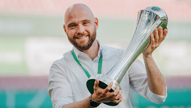 Stephan Lerch hält einen Pokal in der Hand und lacht.