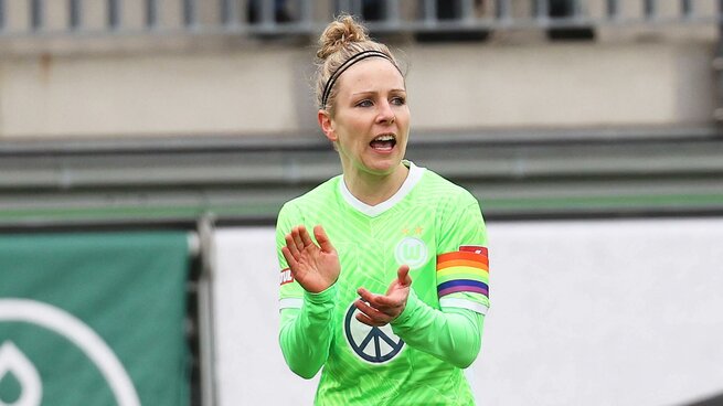 Kathrin Hendrich vom VfL Wolfsburg klatscht auf dem Platz motivierend in die Hände, ihren Oberarm ziert eine Regenbogenbinde.