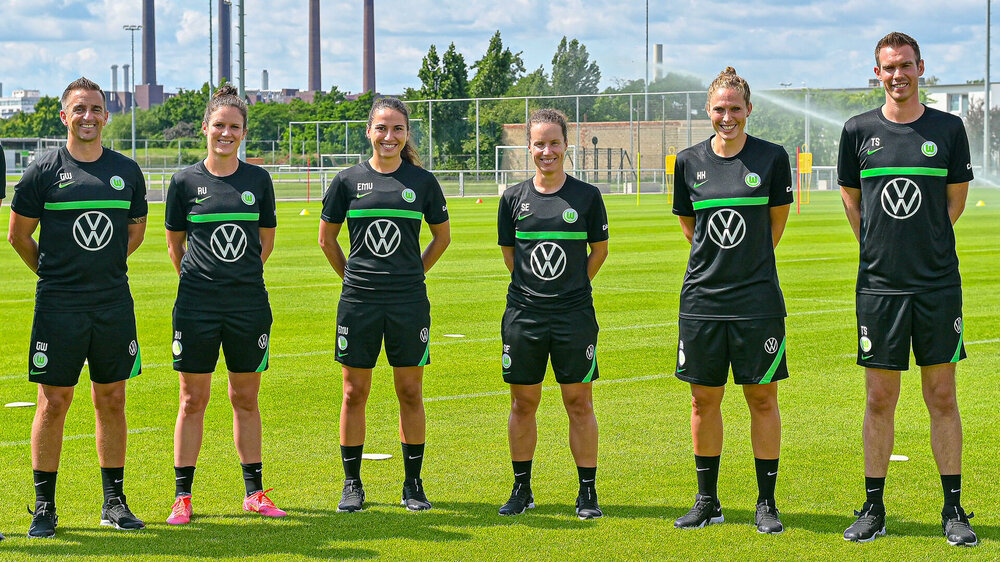 VfL Wolfsburg's Trainerstab der Frauenmannschaft posiert nebeneinander auf dem Trainingsplatz.