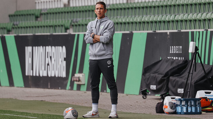 VfL-Wolfsburg-Nachwuchstrainer der U19 Daniel Bauer steht an der Seitenlinie und verschränkt die Arme.