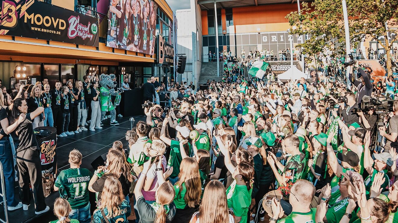 Die Mannschaft des VfL Wolfsburg steht vor einer Menschanmasse vor dem B´moovd.