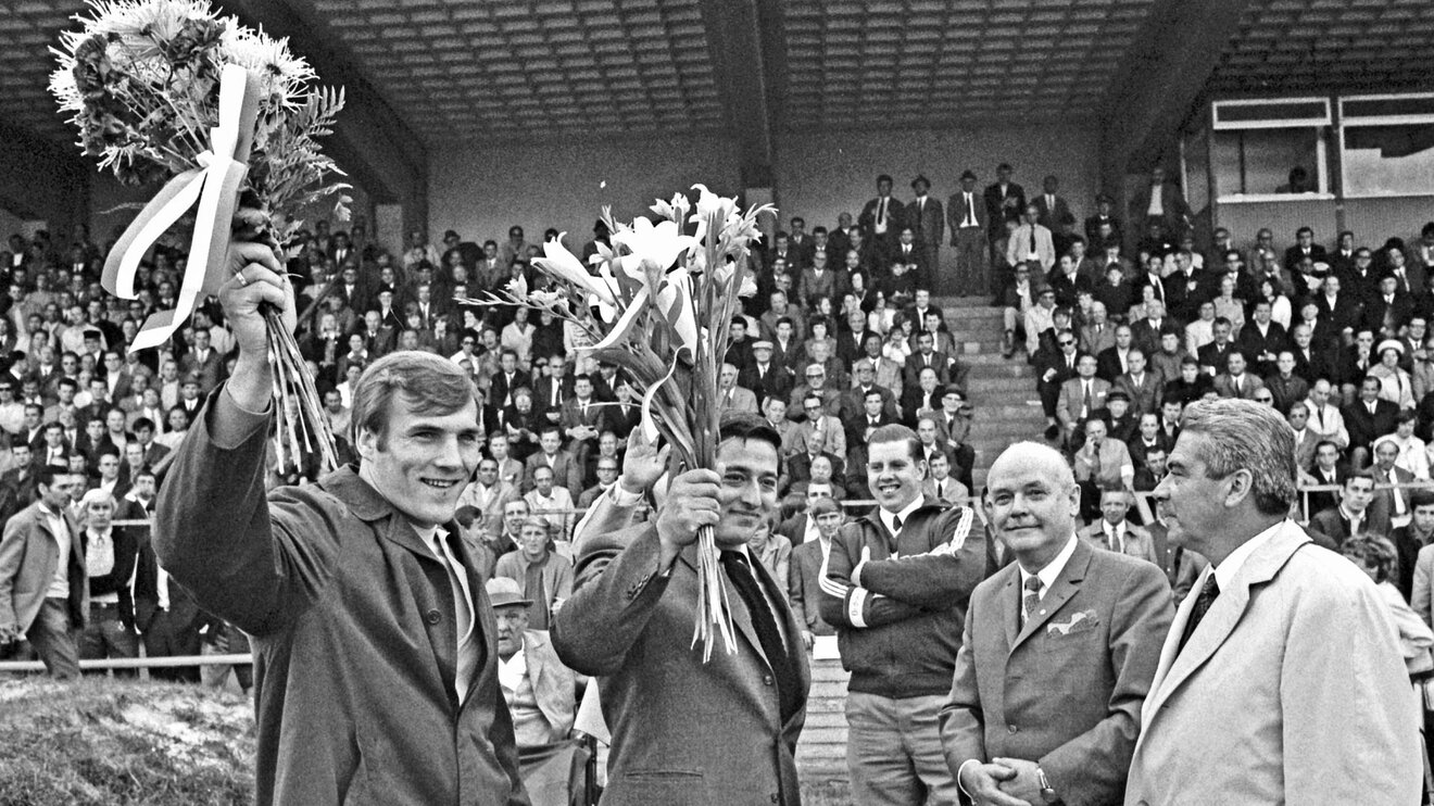 Ehemalige VfL Wolfsburg Spieler halten Blumensträuße auf einer historischen Aufnahme.
