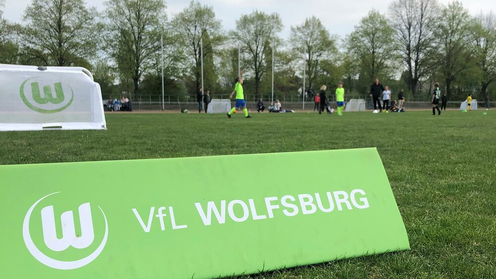 Eine Bande mit Logo und Schrift vom VfL Wolfsburg steht auf dem Platz beim Kinderfußball-Turnier.