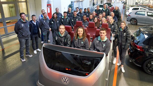 Die Spieler:innen des VfL Wolfsburg machen ein Gruppenfoto im und um das Zugfahrzeug im Werk Wolfsburg.