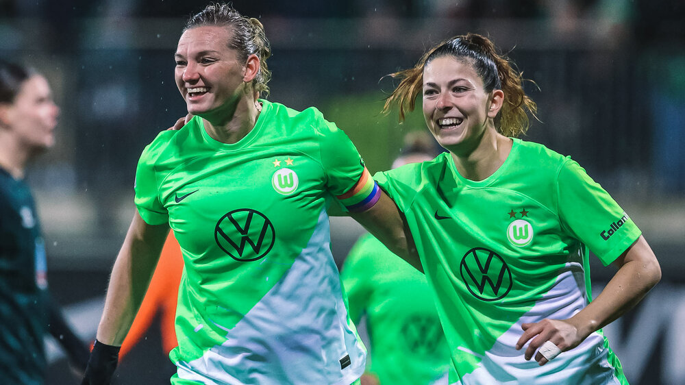 Die beiden VfL-Wolfsburg-Spielerinnen Alexandra Popp und Chantal Hagel laufen freudig Arm in Arm über den Platz.