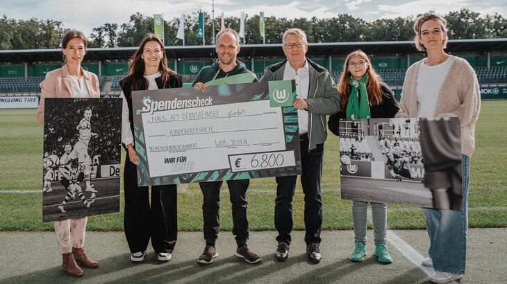 VfL-Wolfsburg-Spielerin Joelle Wedemeyer sowie Fotografin Nina Stiller bekommen einen Spendenscheck in Höhe von 6.800€ überreicht. Sie posieren im AOK Stadion für ein Foto.