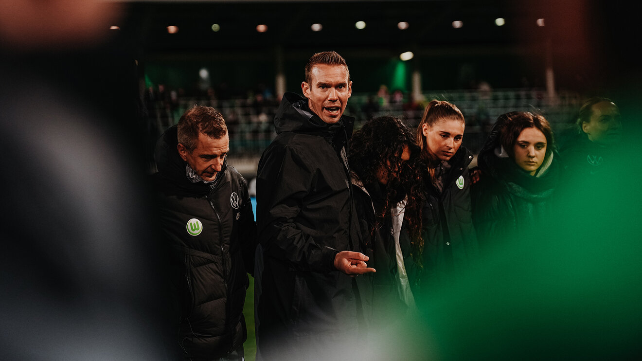 VfL-Wolfsburg-Trainer Tommy Stroot der in einem Kreis mit der Mannschaft steht und spricht.