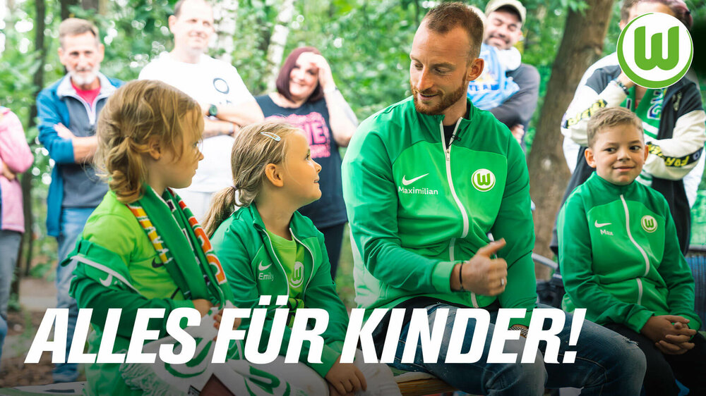Der VfL-Wolfsburg-Spieler Maximilian Arnold sitzt neben Kindern.