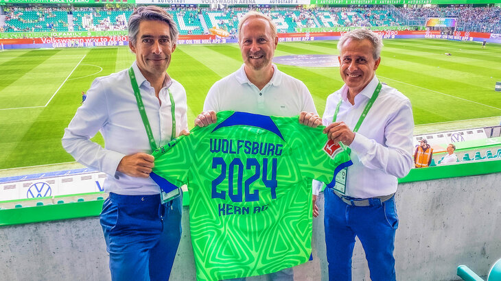 Michael Meeske und Pierre Littbarski halten zusammen mit einem Vertreter der Kern AG ein VfL Wolfsburg-Trikot in der Hand.