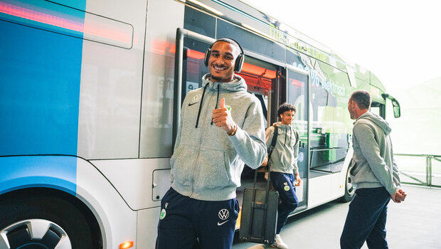 Der VfL Wolfsburg-Spieler Maxence Lacroix steigt lächelnd aus dem E-Bus.