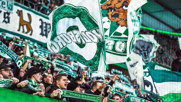 Die Fans des VfL Wolfsburg schwenken Fahnen in der Nordkurve.