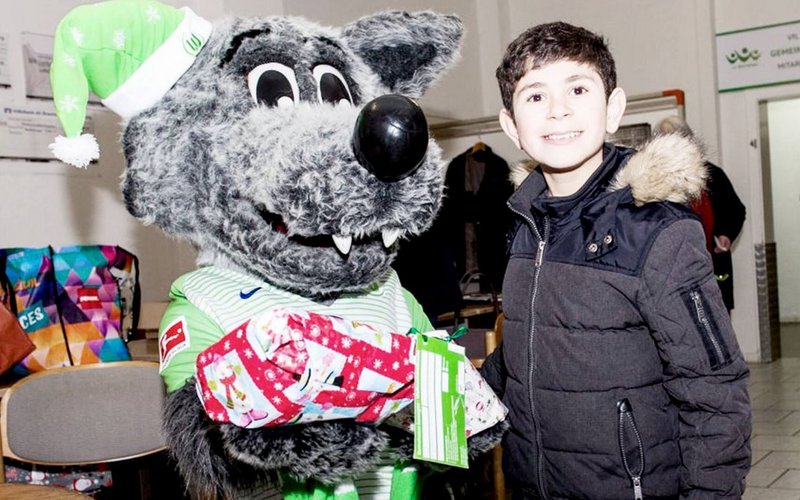 Wölfi hat ein Kind im Arm bei der Weihnachtswunschaktion vom VfL Wolfsburg.