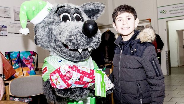 Wölfi hat ein Kind im Arm bei der Weihnachtswunschaktion vom VfL Wolfsburg.