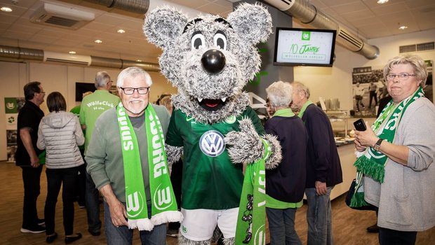 Mitglieder des WölfeClub 55plus vom VfL Wolfsburg machen ein Foto mit Wölfi.