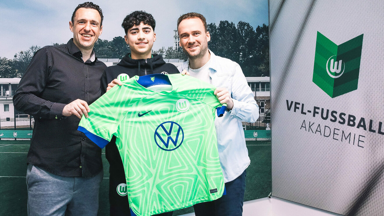 Ein Jugendspieler der VfL-Wolfsburg-Akademie hält ein Trikot in seinen Händen. Im Hintergrund ist die VfL-Fußballwelt zu sehen.