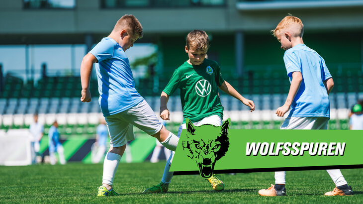 Neben dem Schriftzug "Wolfsspuren" spielen drei Kinder bei der letzten Arenawoche des VfL Wolfsburg gegeneinander.