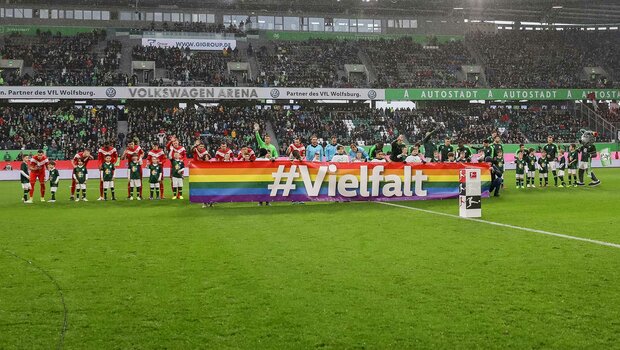 Die Mannschaften halten in der Volkswagen Arena vom VfL Wolfsburg halten zusammen ein Vielfalts-Banner hoch.
