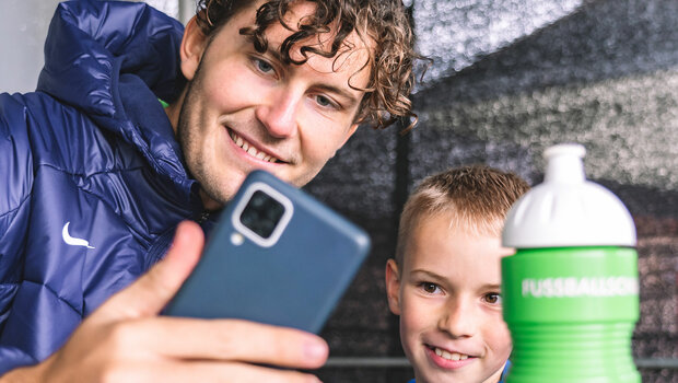 VfL Wolfsburg Spieler Wind macht ein Selfie mit einem kleinen Fan.
