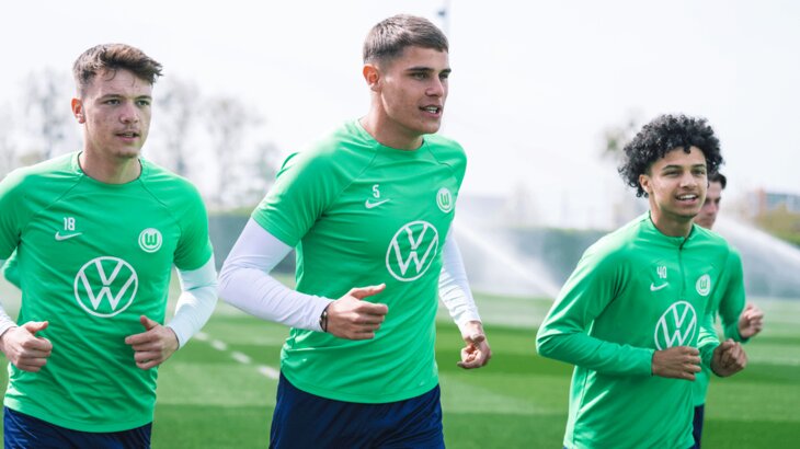 Die drei Spieler des VfL Wolfsburg Pejcinovic, Van de Ven und Paredes laufen sich im Trainingsdress warm.
