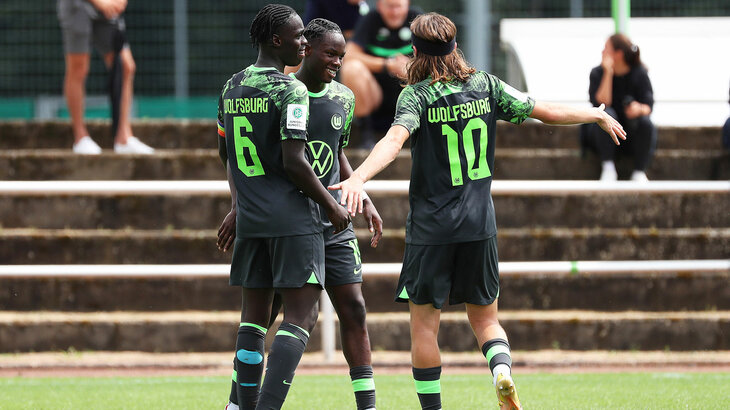 Drei U19-Spieler des VfL Wolfsburg reden auf dem Rasen.