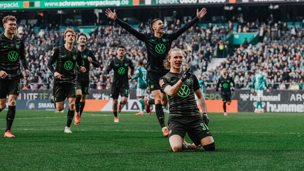 Patrick Wimmer rutscht auf den Knien über den Rasen und jubelt. Hinter ihm laufen weitere VfL-Wolfsburg-Spieler.