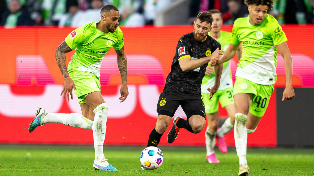 Die VfL Wolfsburg Spieler Nmecha und Paredes setzen sich im Spiel um den Ball gegen einen Gegner durch.