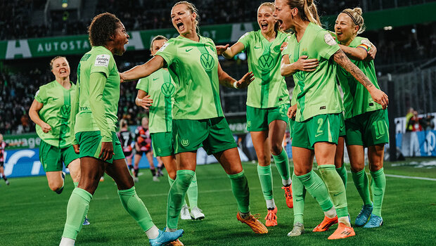 Die Spielerinnen des VfL Wolfsburg stehen auf dem Fußballplatz in der Volkswagen Arena und jubeln miteinander.