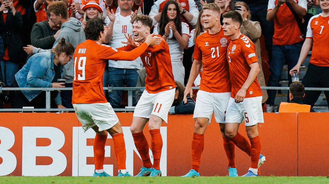 VfL Wolfsburg Spieler Skov Olsen jubelt im Trikot der dänischen Nationalmannschaft mit seinem Kollegen Jonas Wind auf dem Spielfeld.