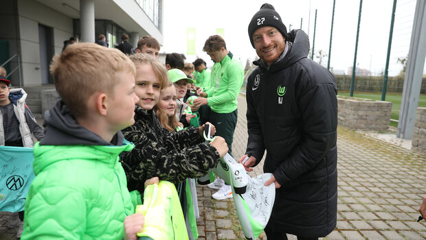 Maximilian Arnold signiert Fanartikel für kleine Fans und lächelt in die Kamera.