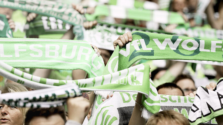 Fans des VfL Wolfsburg halten Vereinsschals in die Höhe. 