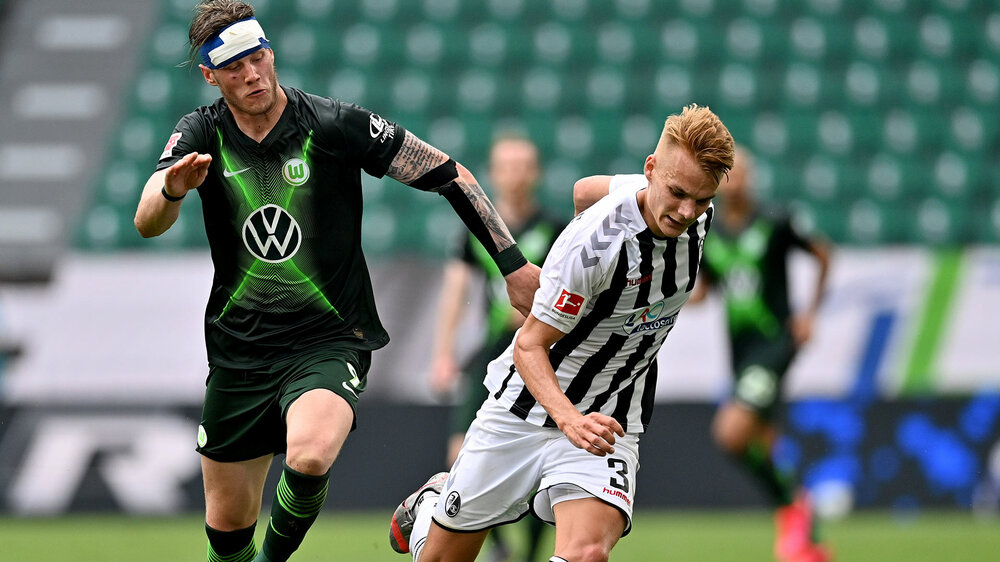 VfL Wolfsburg Spieler Weghorst mit Verband am Kopf im Zweikampf mit einem Gegner aus Freiburg.