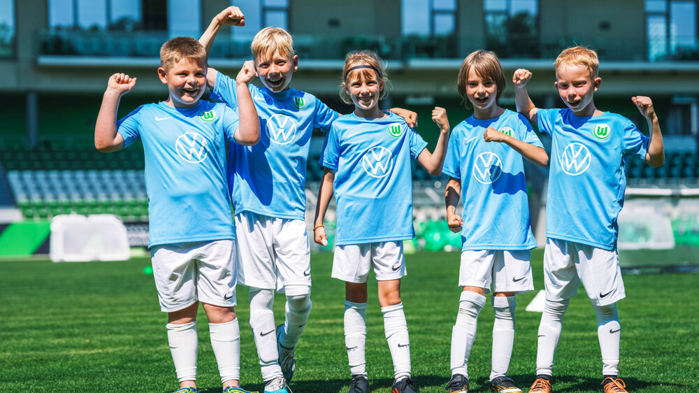 Kinder aus der Fußballschule des VfL Wolfsburg jubeln in ihren Trikots.