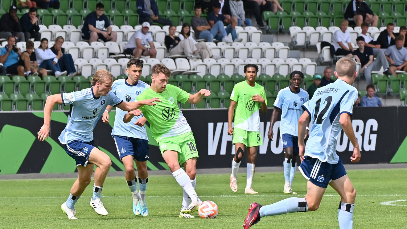 Der VfL Wolfsburg-Spieler aus der U19 steht zwischen gegnerischen Spielern und passt den Ball.