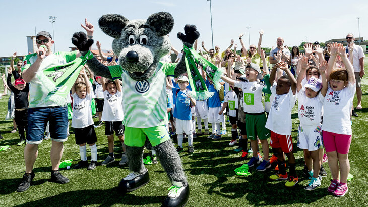 VfL-Maskottchen Wölfi jubelt mit einigen Kindern. 
