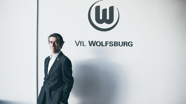 VfL Wolfsburg Geschäftsführer Meeske posiert vor einem Vereinslogo an einer Wand der Volkswagen Arena.