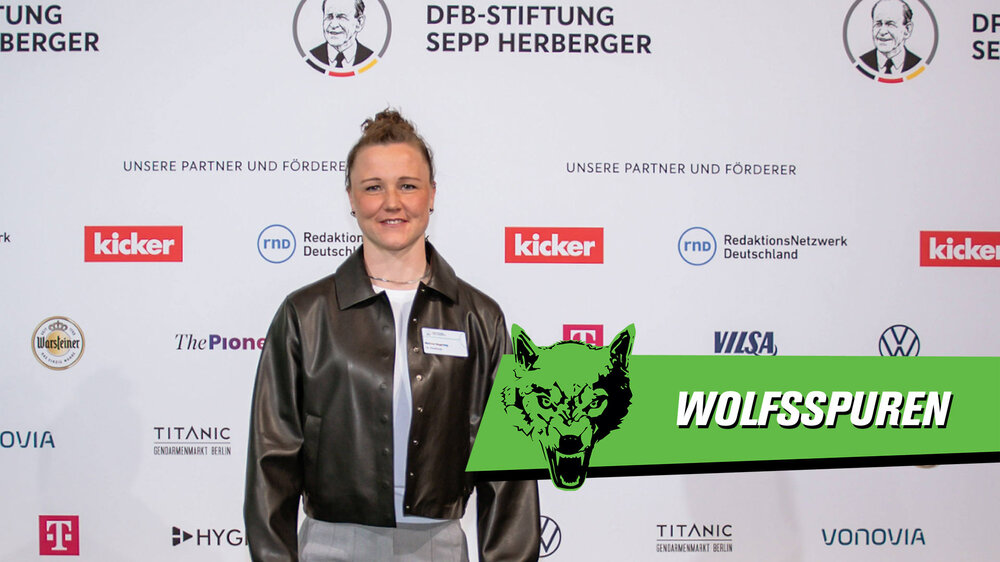 Marina Hegering vom VfL Wolfsburg steht vor einer Fotowand bei den Sepp-Herberger Awards. Auf dem Bild steht der Schriftzug "Wolfsspuren".
