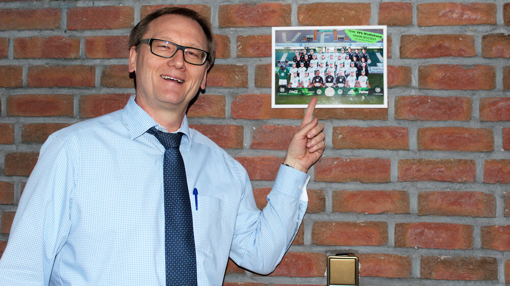 Rüdiger Niehs zeigt lachend auf ein Mannschaftsfoto des VfL. 