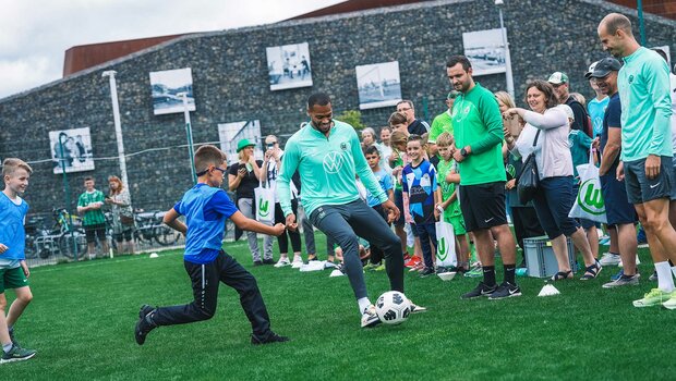 VfL-Wolfsburg-Spieler Lukas Nmecha spielt mit einem Kind Fußball beim Familienfest.