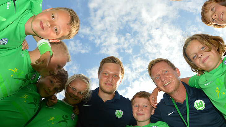 VfL Wolfsburg Fußballschuel - Kinder stehen mit dem Team im Kreis und lachen. 