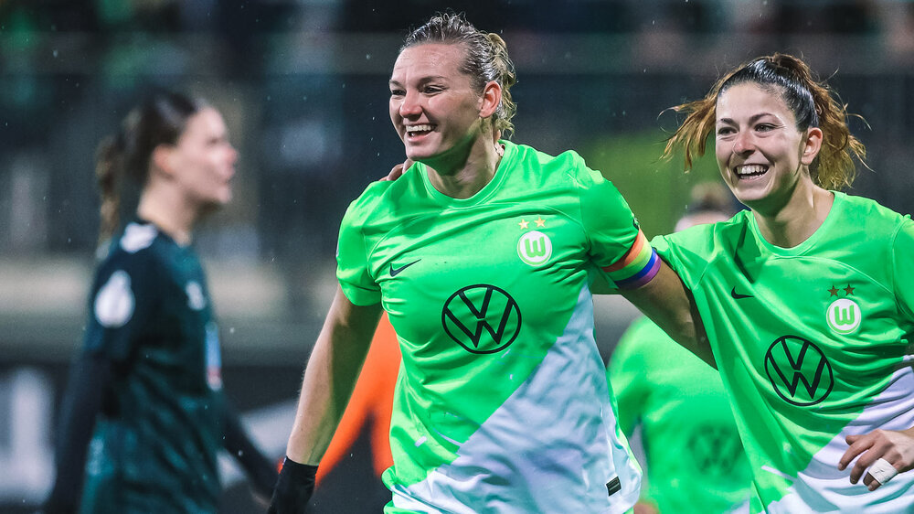 VfL-Wolfsburg-Spielerin Alexandra Popp läuft Arm in Arm mit Chantal Hagel und lacht.