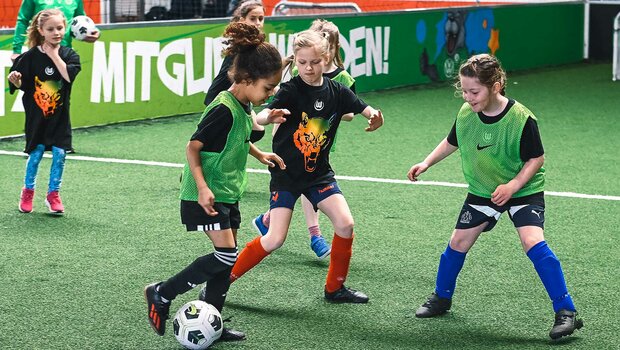 Drei Mädchen vom Girls Day im Kampf um den Ball im Bolzwerk des VfL Wolfsburg.