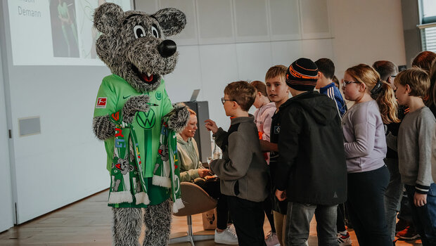 Wölfi vom VfL Wolfsburg steht vor einer Schlange von Kindern und gibt Autogramme.