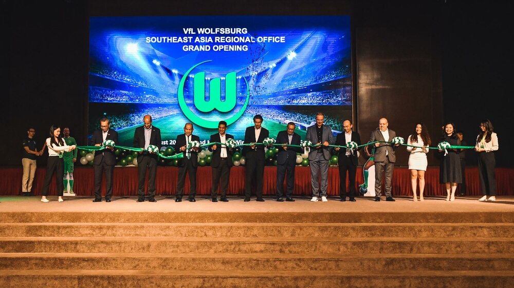 Bei der Eröffnung des VfL-Wolfsburg-Büros in Malaysia zerschneiden meherer Personen ein grünes Band auf der Bühne.