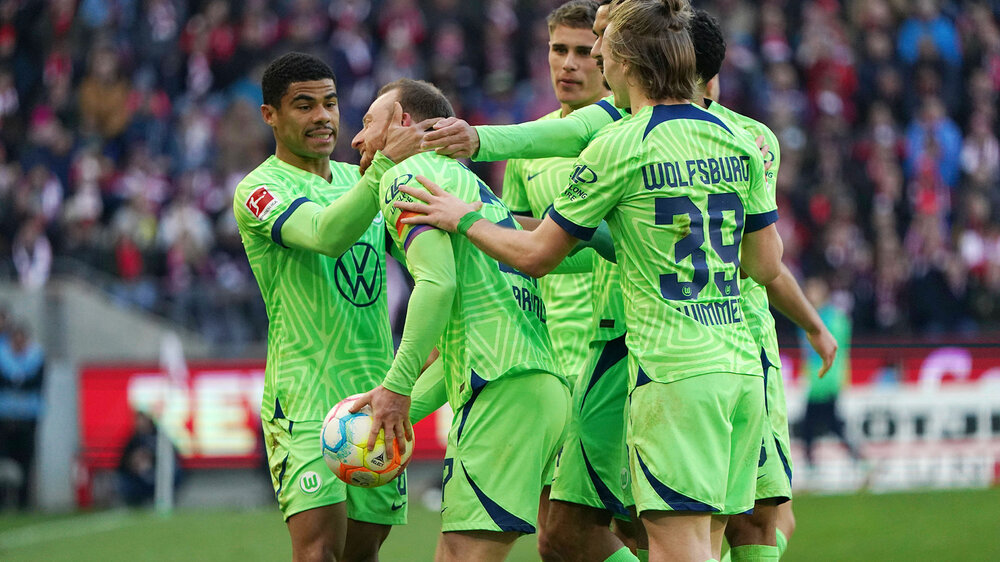 The VfL Wolfsburg team embraces scorer Maximilian Arnold after his penalty goal.