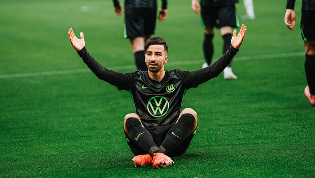 VfL-Wolfsburg-Spieler Mohammed Amoura sitzt auf dem Boden und hebt die Arme.