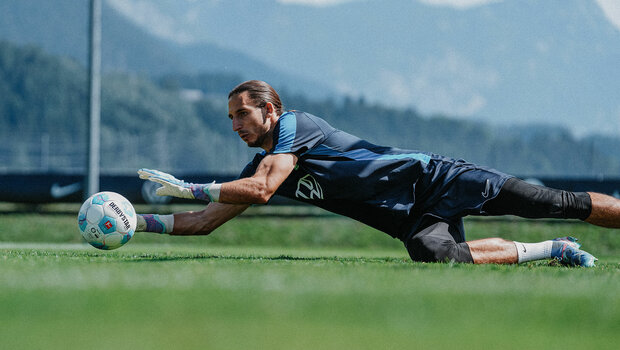 VfL-Wolfsburg-Spieler Kamil Grabara hechtet zu einem heranfliegenden Ball hin.