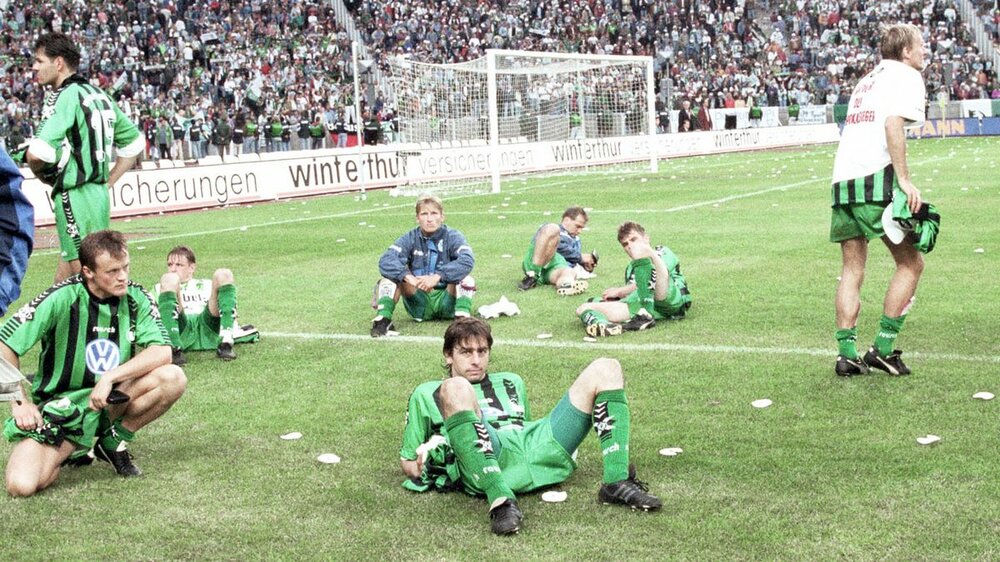 VfL Wolfsburg-Spieler sitzen nach einem Spiel auf dem Rasen.