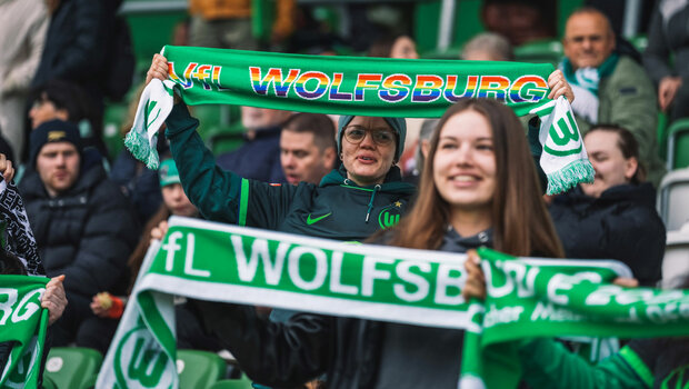 Ein weiblicher VfL Wolfsburg Fan hält einen Vielfaltsschal in die Höhe.