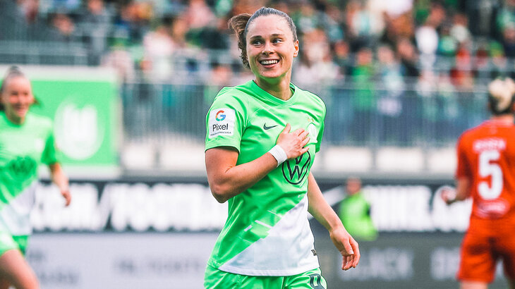 VfL-Wolfsburg-Spielerin Ewa Pajor läuft über den Platz, legt die rechte Hand aufs Herz und lächelt.